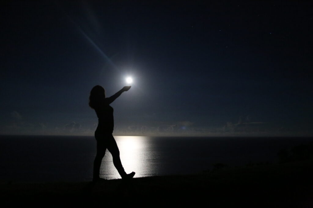 Woman silhouette appearing to hold the full moon in her hand on a moonlit night at Ishigaki Island — moon phase affects stargazing conditions