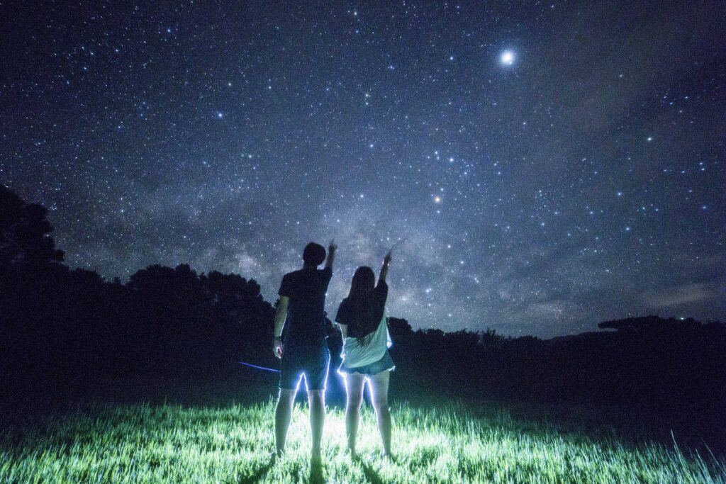 Couple looking up at the starry sky in a grass field at Nagareboshi no Oka, Ishigaki Island
