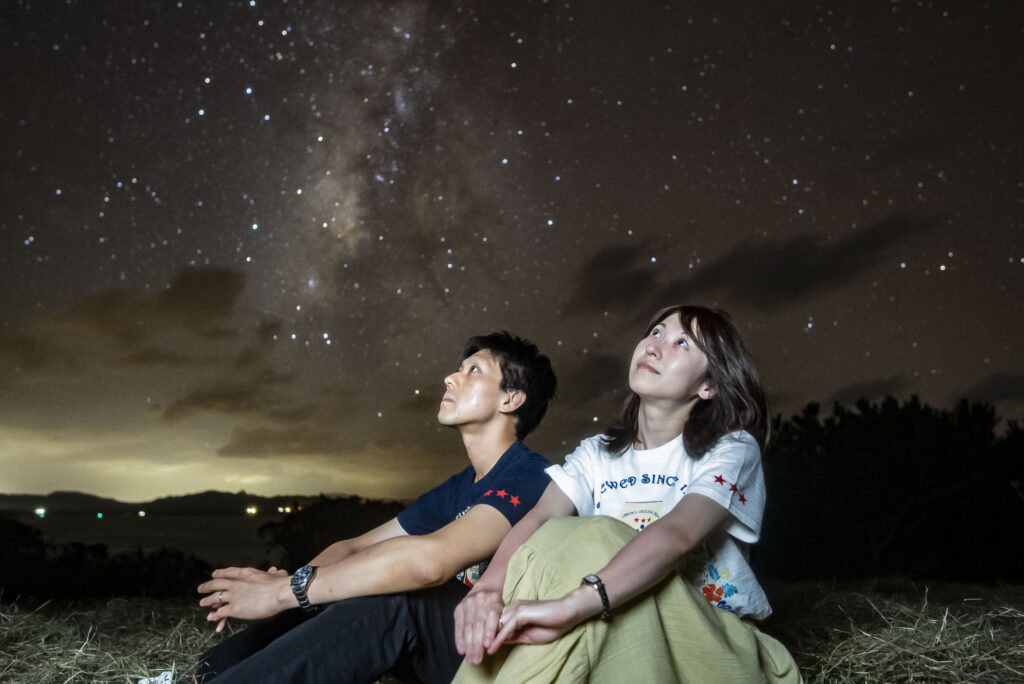 Young couple sitting and looking up at the Milky Way during stargazing at Nagareboshi no Oka, Ishigaki Island