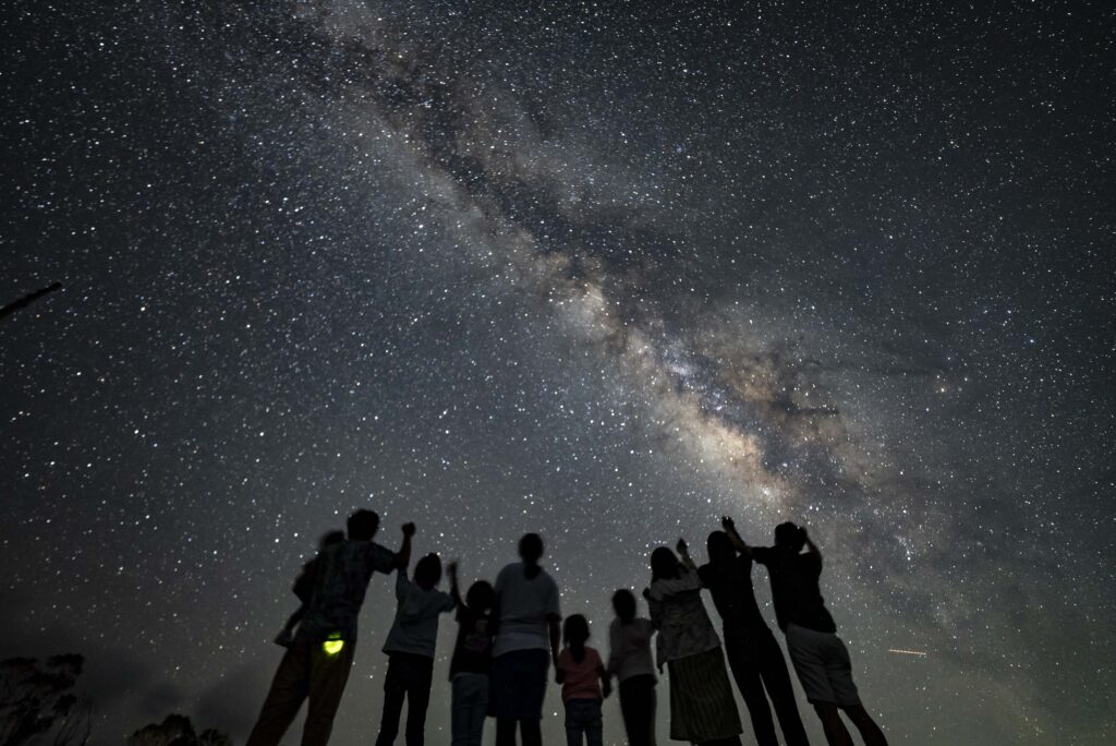 Stargazing tour group raising hands under the Milky Way at beach, Nagareboshi no Oka, Ishigaki Island